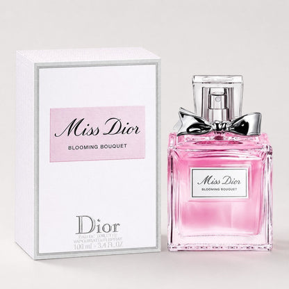 Perfume Dior Miss Dior Blooming Bouquet de Ricky Luxury con frasco de cristal rosa y lazo plateado junto a su caja.