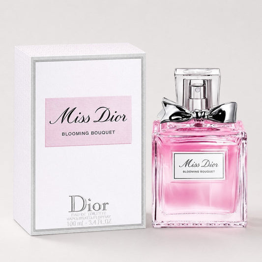 Perfume Dior Miss Dior Blooming Bouquet de Ricky Luxury con frasco de cristal rosa y lazo plateado junto a su caja.