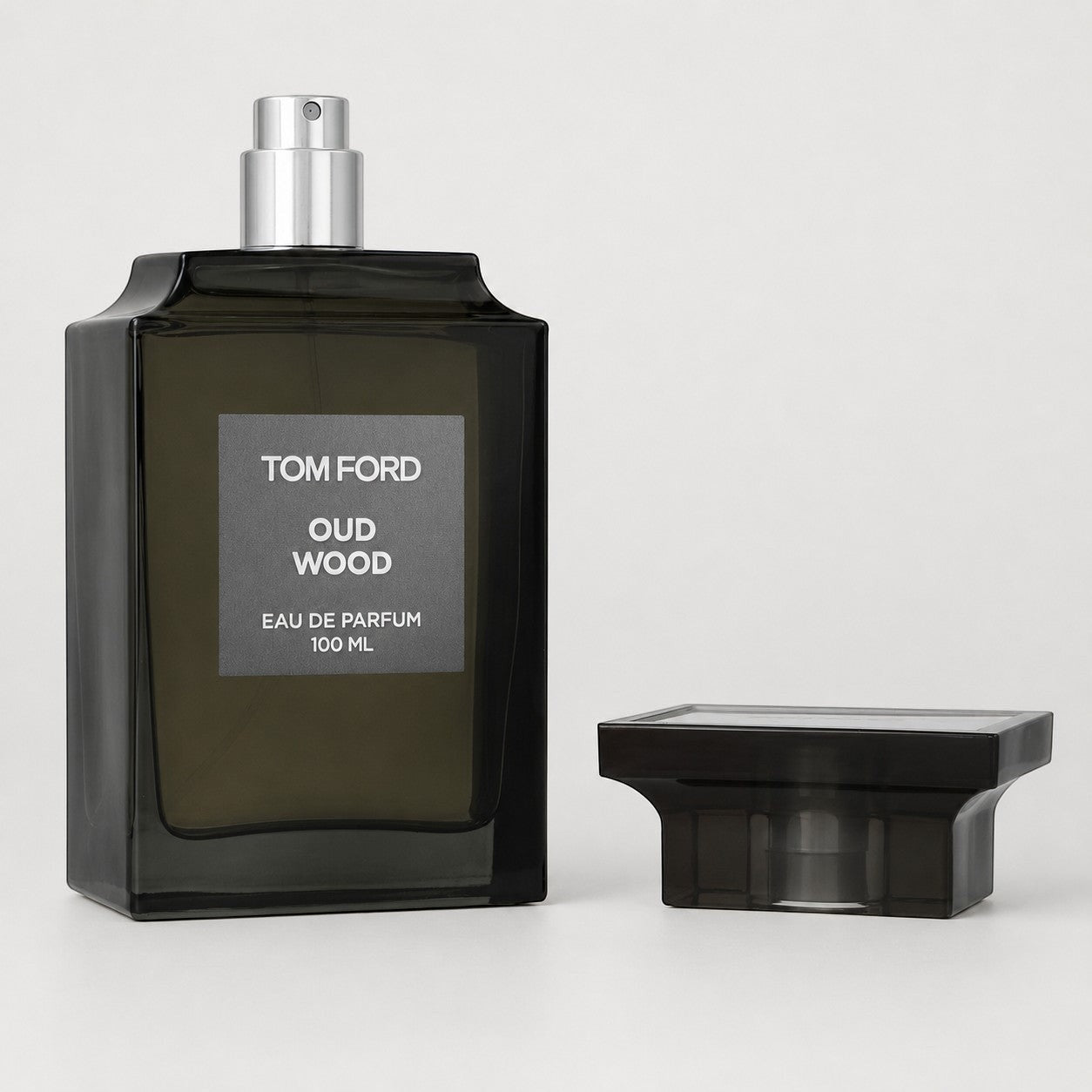 Perfume Tom Ford Oud Wood de Ricky Luxury en frasco de vidrio oscuro con tapa negra sobre fondo gris claro